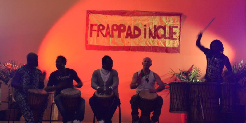 Concert de percussion avec plusieurs artistes sur scène, devant une banderole "FRAPPAD INOLE".