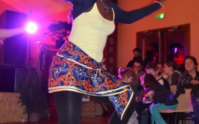 Danseuse en tenue colorée se produisant sur scène, avec un public attentif en arrière-plan.