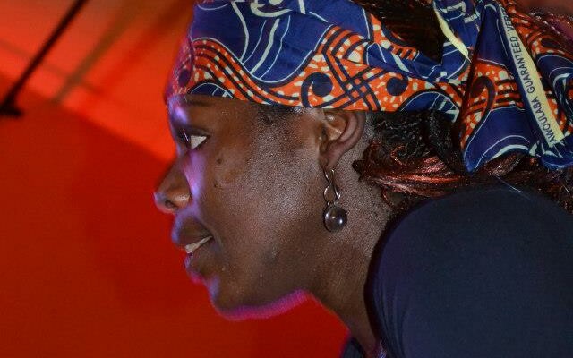 Femme avec un foulard coloré, observant un événement dans une ambiance lumineuse.