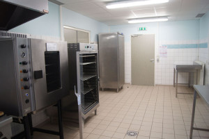 Cuisine professionnelle avec équipements en acier inoxydable, incluant un four et un réfrigérateur.