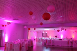 Salle de réception décorée avec des lanternes colorées et un éclairage rose pour un événement festif.