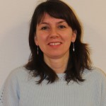 Portrait d'une femme souriante portant un pull clair, prise sur fond neutre.