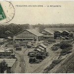 Image historique de la briqueterie à Feuguerolles-sur-Orne, montrant des bâtiments et des matériaux empilés.