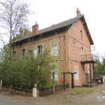 Maison en briques avec un balcon, entourée de végétation, située à Feuguerolles-Bully, près de Caen.