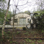 Ancien bâtiment avec inscription "Le béton vibré", entouré de verdure et de tuyaux empilés dans la commune de Feuguerolles-Bully.