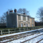 Maison rénovée à Feuguerolles-Bully, entourée de nature avec des rails de chemin de fer poussiéreux au premier plan.