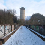 Vue d'un chemin enneigé menant à un réservoir, bordé de graffitis et entouré d'une forêt.