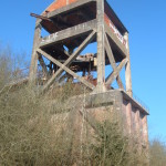 Vue d'une structure industrielle délaissée entourée d'arbres, sous un ciel bleu.
