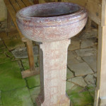 Baptistère en pierre décoratif dans un coin d'une église, sur un sol en pavés et des bancs en bois.