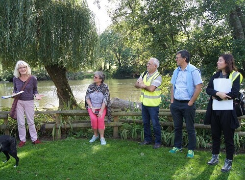 Groupe de personnes discutant près d'une rivière, avec des arbres et de la verdure en arrière-plan.