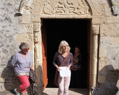 Visite guidée devant une porte décorée d'une église, avec des femmes discutant à l'extérieur.