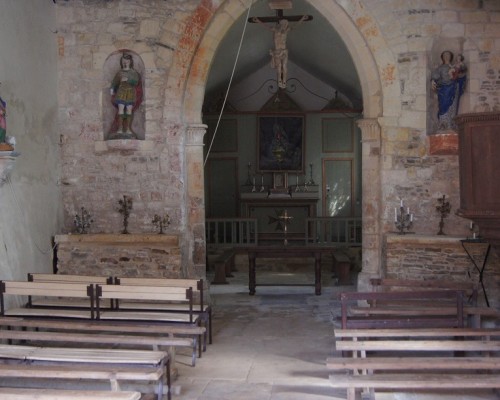 Intérieur de l'église de Feuguerolles-Bully, avec bancs, autel et sculptures décoratives.