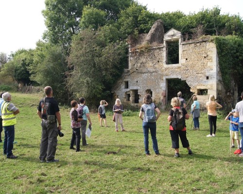 Visite d'un groupe devant une ruine historique à Feuguerolles-Bully, entourée de verdure.