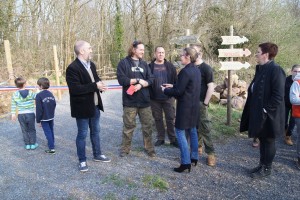 Inauguration d'un parc communal avec des visiteurs et des intervenants, entourés de panneaux directionnels et de verdure.