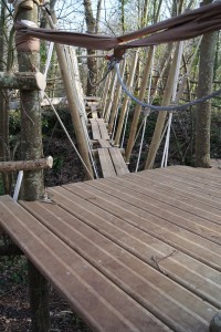 Pont suspendu en bois situé dans un espace naturel à Feuguerolles-Bully, entouré d'arbres.