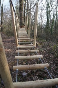 Passerelle en bois suspendue entre des arbres, située dans une forêt près de Feuguerolles-Bully.