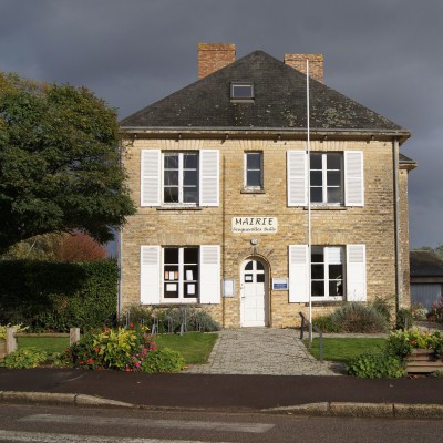Mairie de Feuguerolles-Bully, bâtiment en pierre avec jardin fleuri, sous un ciel nuageux.