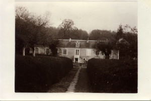 Vue d'une maison rurale entourée de haies, avec un chemin pavé menant à l'entrée, dans un cadre naturel paisible.