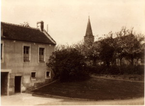 Ancien bâtiment rural avec un jardin et un clocher d'église en arrière-plan, représentant Feuguerolles-Bully.