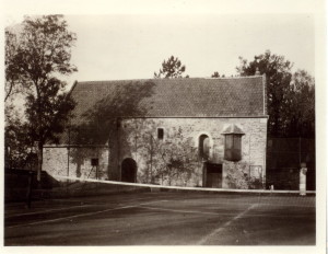Ancien bâtiment en pierre avec un toit en ardoise, entouré d'un terrain de tennis, à Feuguerolles-Bully.