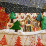 Maison et arbres en tissu, décorations artisanales sur fond neigeux, représentant un paysage rural chaleureux.