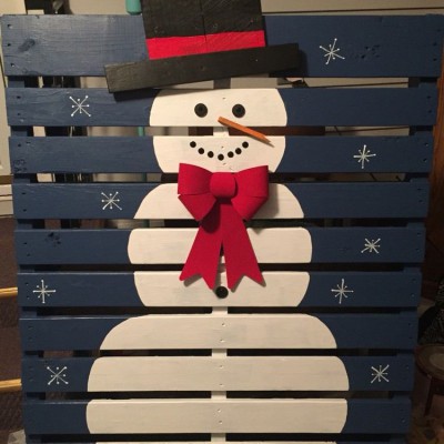 Bonhomme de neige décoratif en bois, avec chapeau noir, écharpe rouge et flocons de neige sur fond bleu.