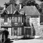 Maison traditionnelle en pierre et colombages à Feuguerolles-Bully, avec un jardin verdoyant.