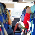 Passagers à bord d'un bus, vue de l'arrière montrant des sièges bleus et des personnes en train de voyager.