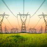 Lignes haute tension sur un champ verdoyant à Feuguerolles-Bully, avec un ciel dégradé au crépuscule.