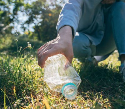 Personne ramassant une bouteille en plastique dans un champ, symbolisant l'engagement pour l'environnement à Feuguerolles-Bully.