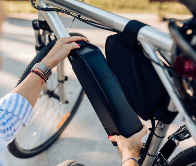 Une personne installe une batterie sur un vélo électrique dans un cadre rural ensoleillé.