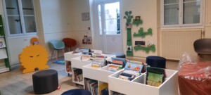 Intérieur d'une bibliothèque avec étagères de livres, fauteuils colorés et un décor ludique pour enfants.