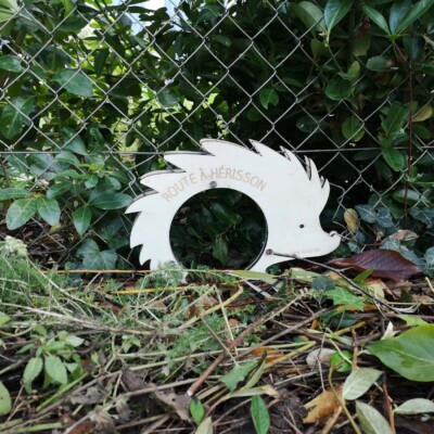Panneau en bois sculpté représentant un hérisson, indiquant la "Route à Hérisson" entouré de végétation.