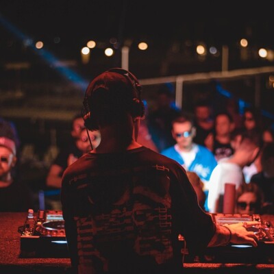 DJ en performance devant une foule dans un ambiance nocturne avec des lumières colorées.