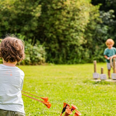 Enfants jouant à l'arc et à des jeux de plein air dans une verdure ensoleillée.