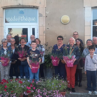 Groupe de villageois devant la médiathèque, portant des fleurs, lors d'un événement communautaire à Feuguerolles-Bully.