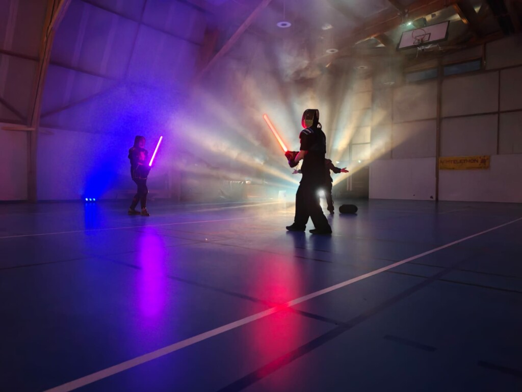 Démonstration de combat avec des sabres laser dans une salle, éclairée par des jeux de lumière colorés.