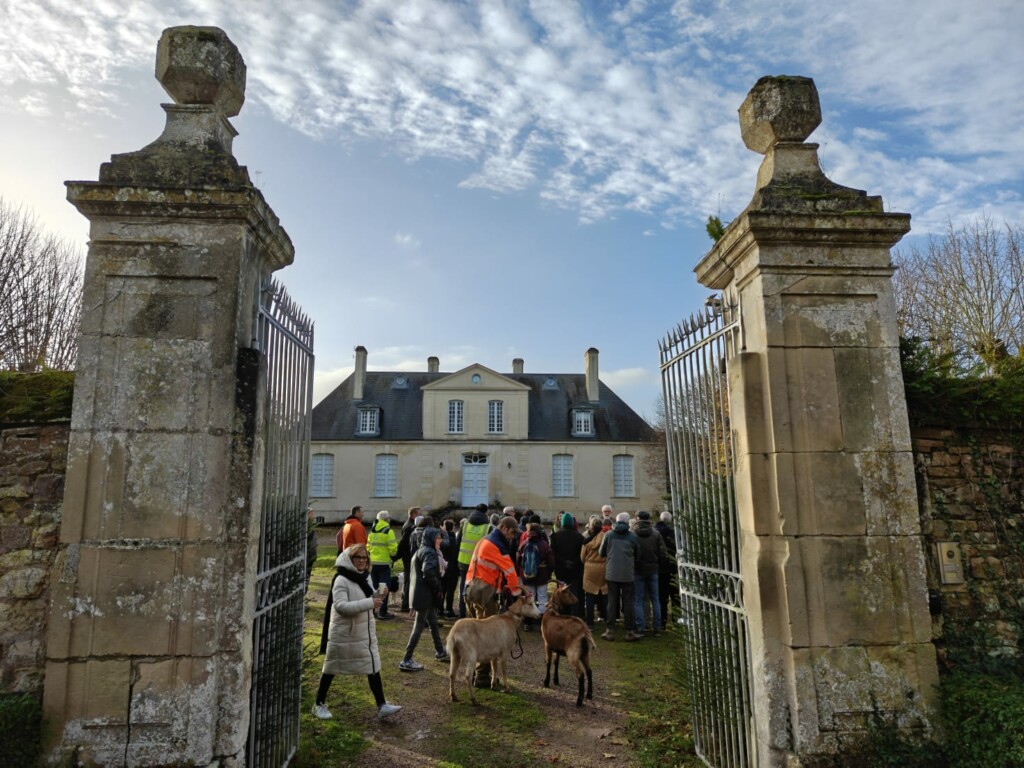Visite d'un château à Feuguerolles-Bully, avec un groupe de personnes et des animaux, sous un ciel partiellement nuageux.