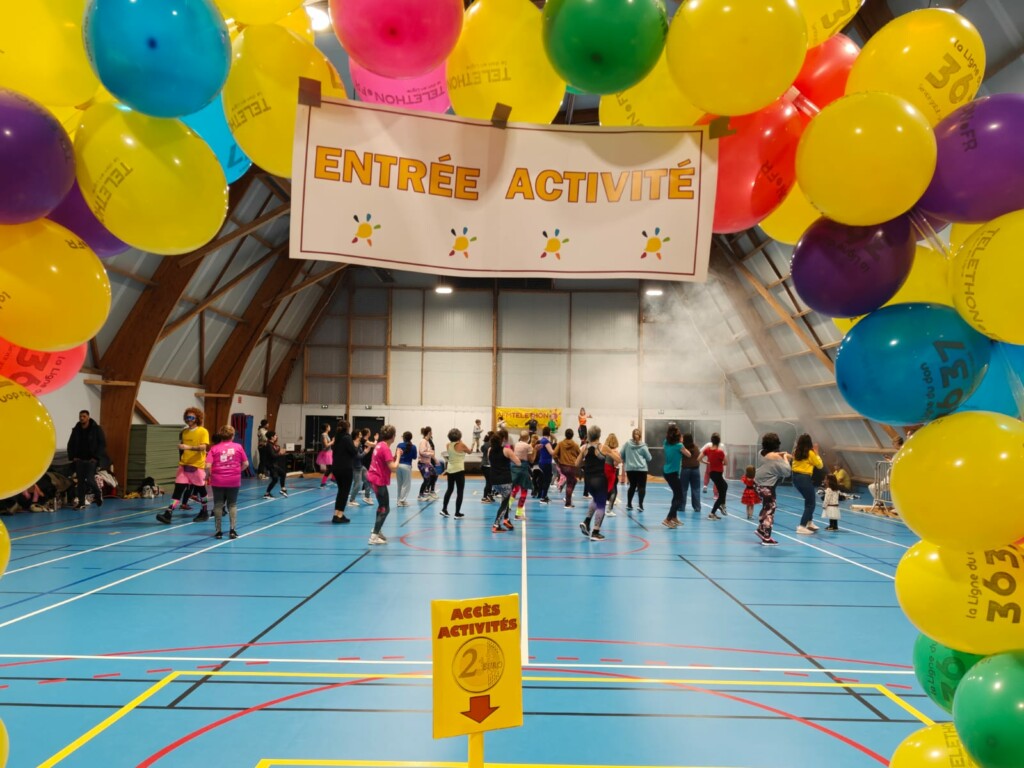 Enfants et adultes participant à une activité sportive sous un arc de ballons, dans une salle de sport à Feuguerolles-Bully.