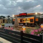 by_silo Snack avec terrasse fleurie à Feuguerolles-Bully, sous un ciel nuageux, offrant un cadre convivial.