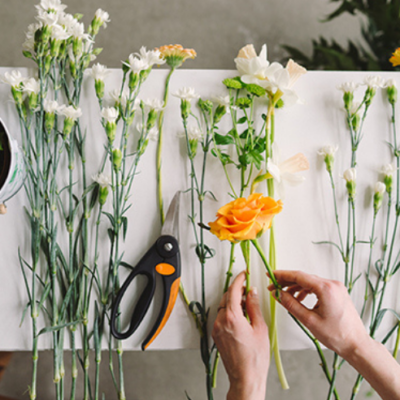 Fleurs colorées et outils de jardinage sur une table, avec des mains en train d'arranger un bouquet.