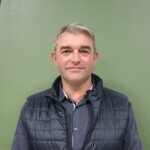 IMG_2532b Portrait d'un homme en veston noir devant un mur vert, représentant un membre de la commune de Feuguerolles-Bully.