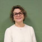 IMG_2535b Portrait d'une femme souriante, portant des lunettes, sur fond vert.