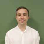 IMG_2540b Homme souriant en chemise blanche sur fond vert.