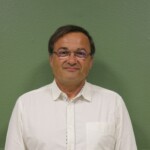 IMG_2542b Portrait d'un homme souriant en chemise blanche, sur fond vert, représentant la commune de Feuguerolles-Bully.