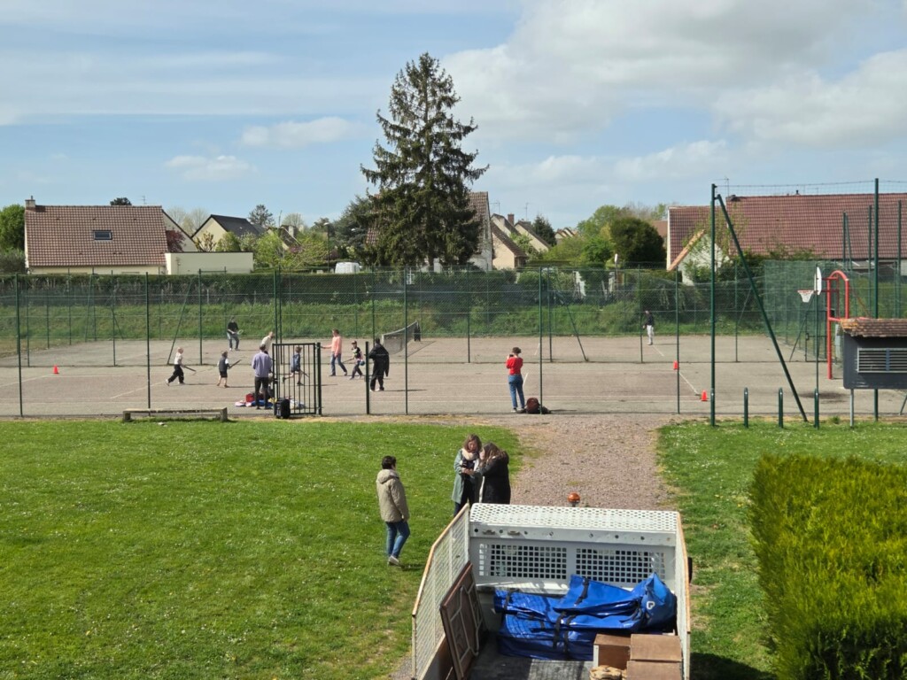 Enfants jouant sur un terrain de sport à Feuguerolles-Bully, avec des habitations en arrière-plan.