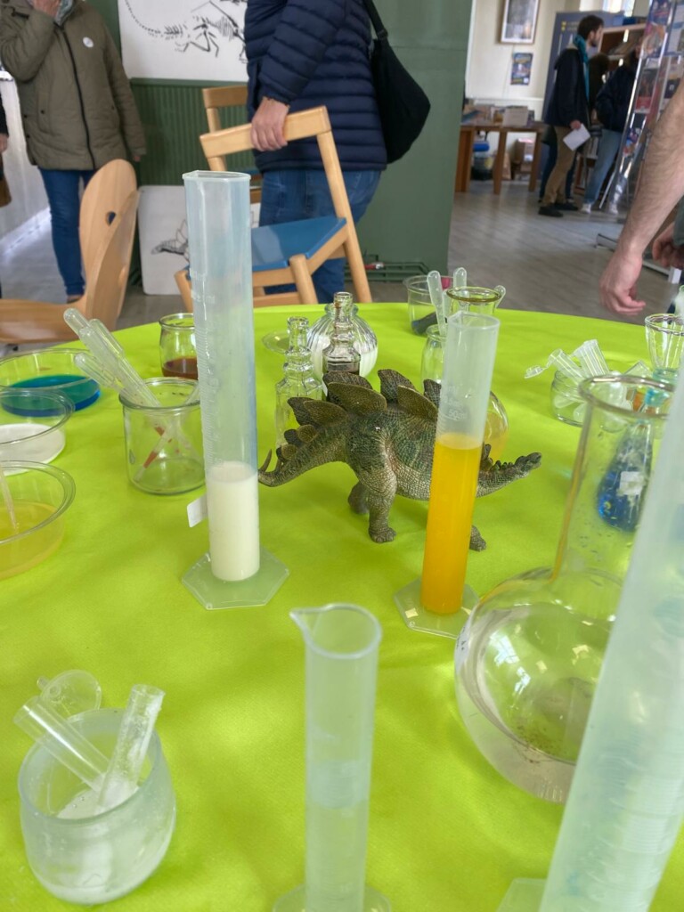 Table d'expérimentation avec des fioles colorées et une figurine de dinosaure, dans un cadre animé.