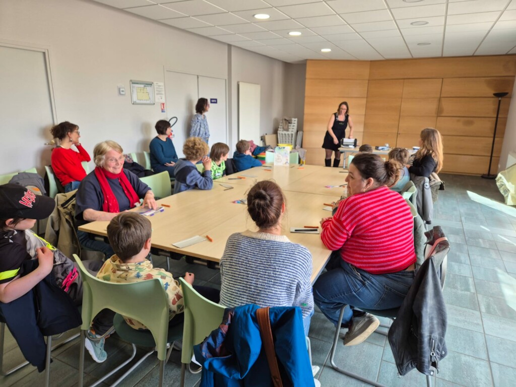 Réunion conviviale à Feuguerolles-Bully, avec des enfants et adultes autour d'une table, discussion et activités en cours.