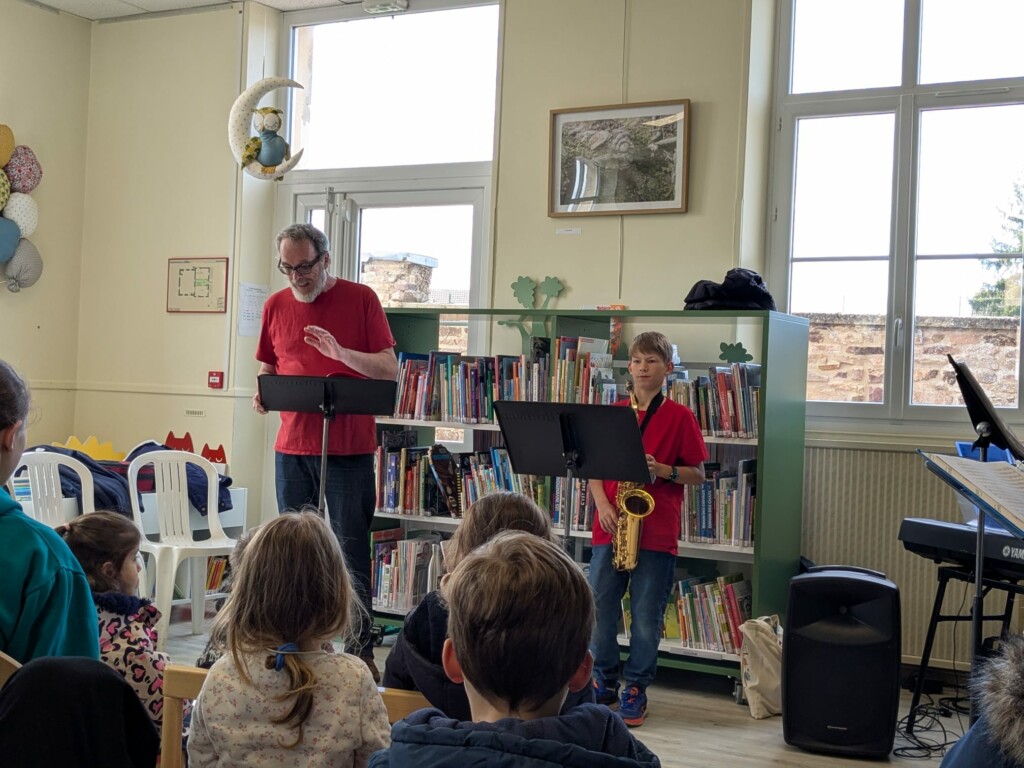 Un homme et un garçon jouent de la musique dans une bibliothèque, devant un public attentif.