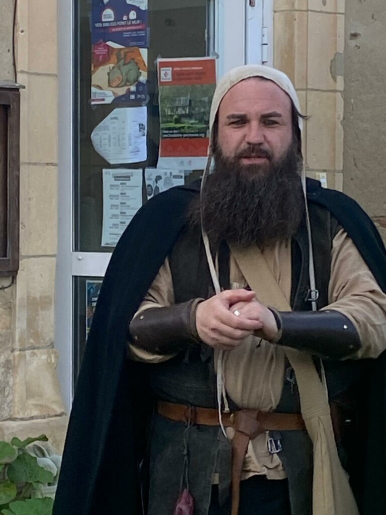 Homme vêtu d'une tenue médiévale, debout devant une fenêtre avec des affiches, à Feuguerolles-Bully.